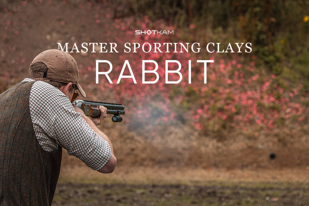 Side view of a clay shooter tracking a rolling rabbit target on a sporting clays course.