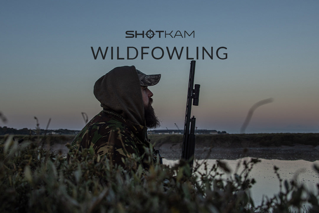 Morning wildfowling on the UK foreshore, a hunter waits in camouflage with his shotgun for ducks at dawn.