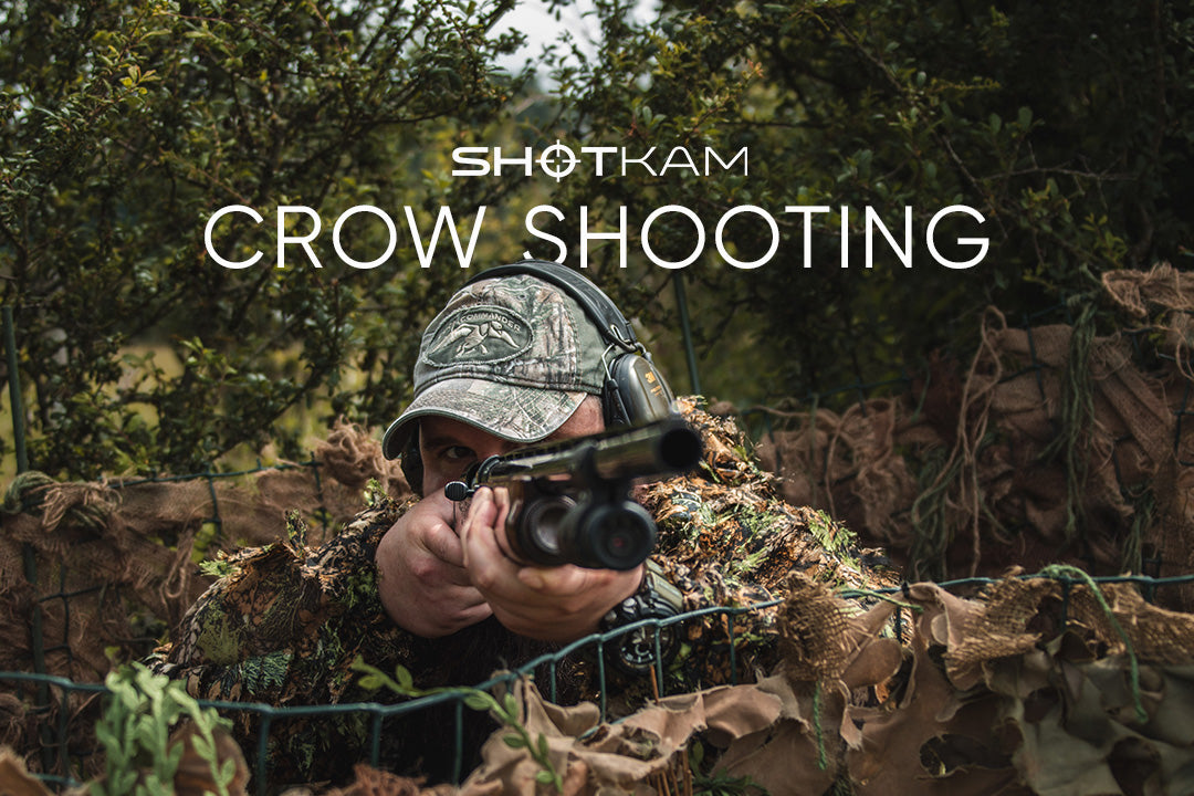 A man in camouflage gear and hat aiming a shotgun while hidden in a blind, showcasing ShotKam crow shooting.