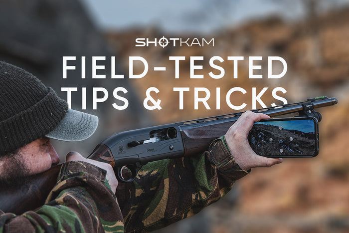 Clay shooter with a ShotKam attached beneath the shotgun barrel, analysing shot placement on a smartphone at the range.