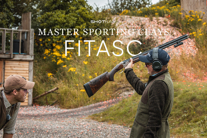 Outdoor shooting scene featuring FITASC athletes mid-conversation, with one displaying shotgun and ShotKam setup.