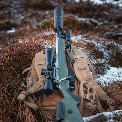 Bolt-action rifle with a ShotKam Gen 4 mounted using the Moderator Mount, resting on a backpack in a rugged, outdoor setting. Ideal for UK hunters and marksmen capturing high-definition shooting footage.