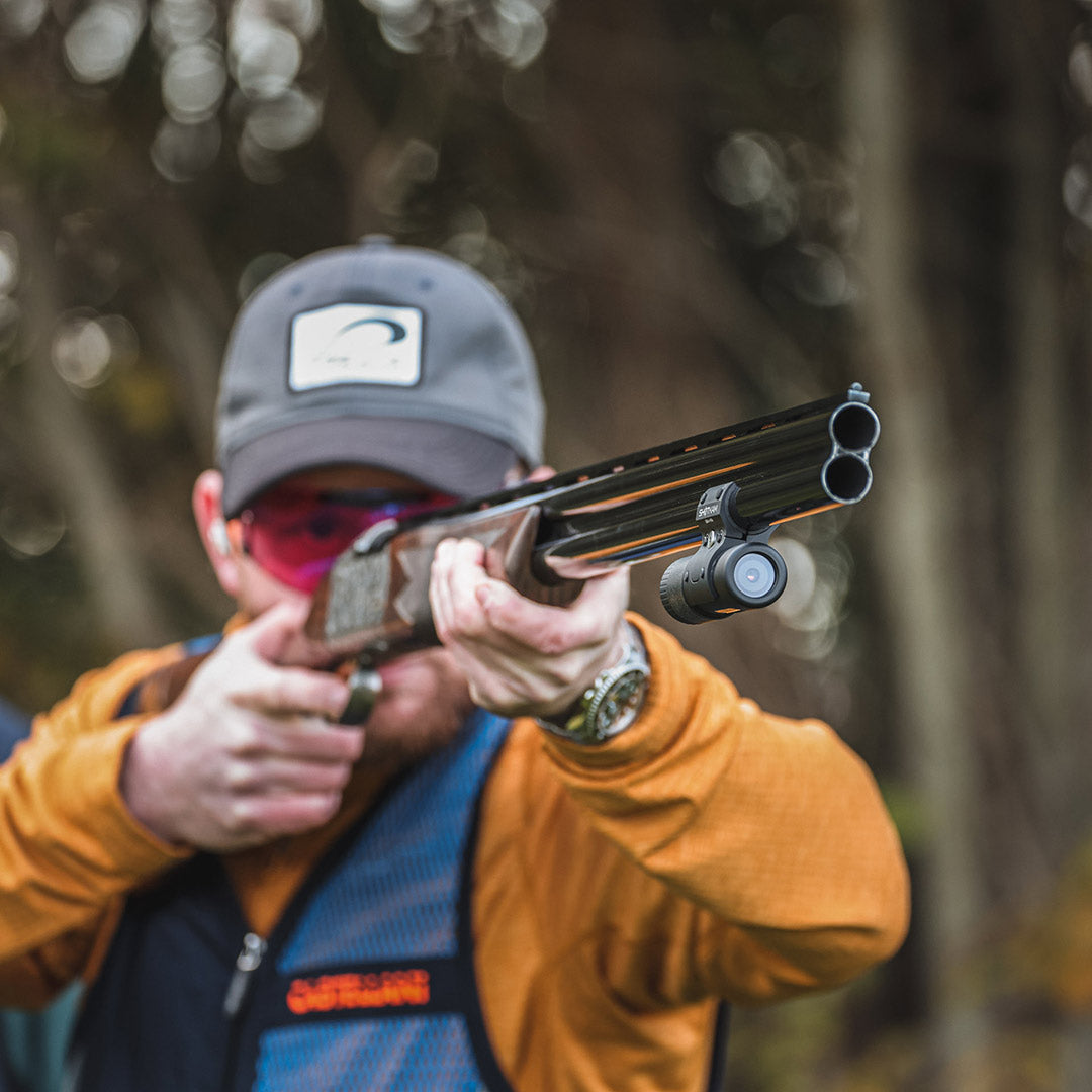 A competitive shooter in the UK, dressed in shooting gear, aims down the barrel of a shotgun fitted with the ShotKam Gen 4 Mini. Ideal for training in clay pigeon shooting, game shooting, and skeet.