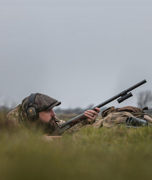 Hunter in camouflage gear with a rifle in a grassy field